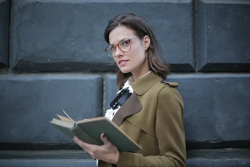 Woman wearing eyeglasses while carrying a book
