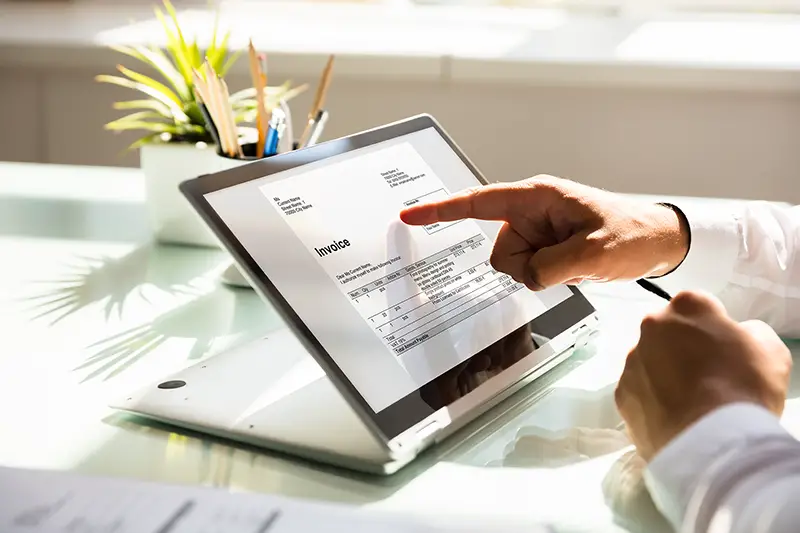 Close-up of a businessman's hand examining invoice on laptop