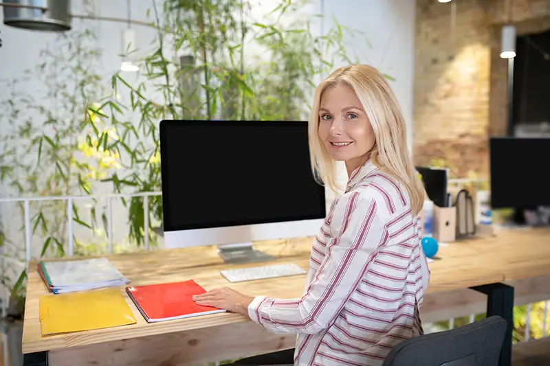 Blonde woman sitting at desk in front of screen