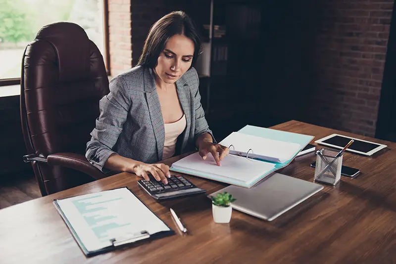 Successful woman in a gray checkered jacket checks using black calculator