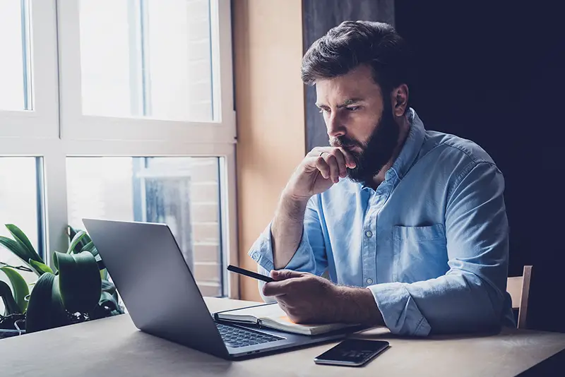 Young serious bearded man in blue shirt working on desktop.