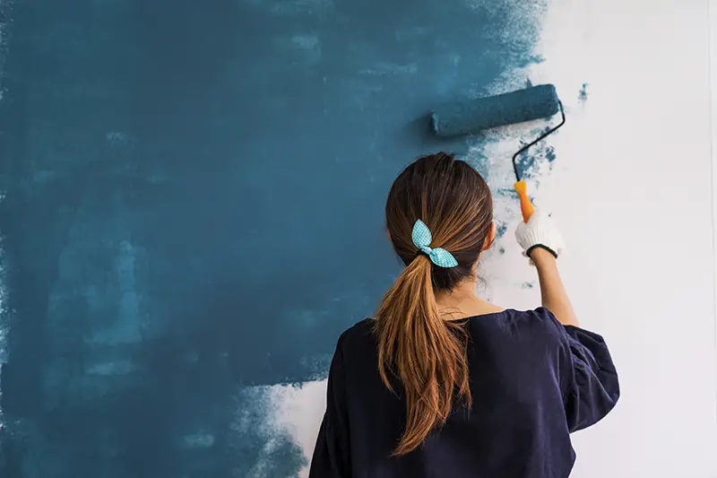 Young asian happy woman painting interior wall with paint roller in new house, Home decoration concept