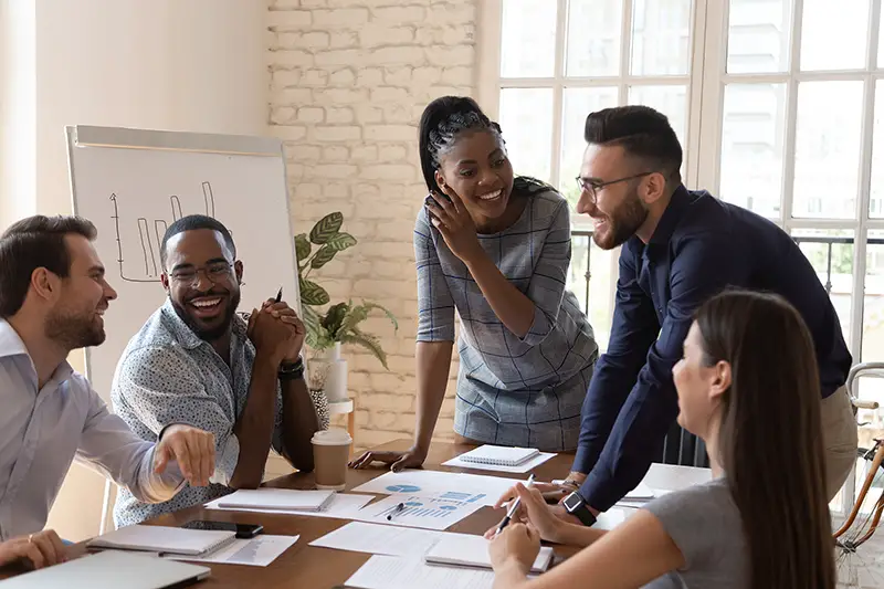 Happy friendly multiracial business team laughing working together at corporate briefing gathered at table