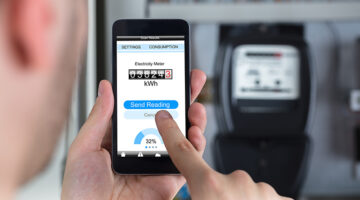 Close-up Of A Man's Hand Holding Mobile Phone Reading Electric Meter