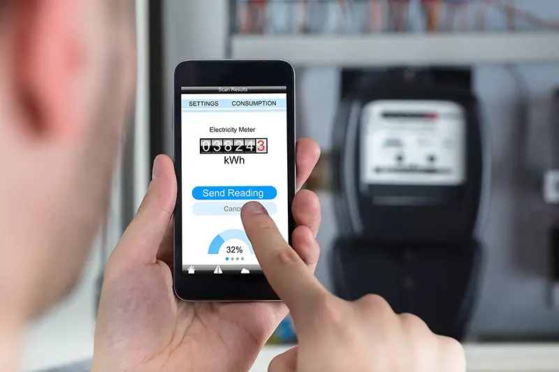 Close-up Of A Man's Hand Holding Mobile Phone Reading Electric Meter