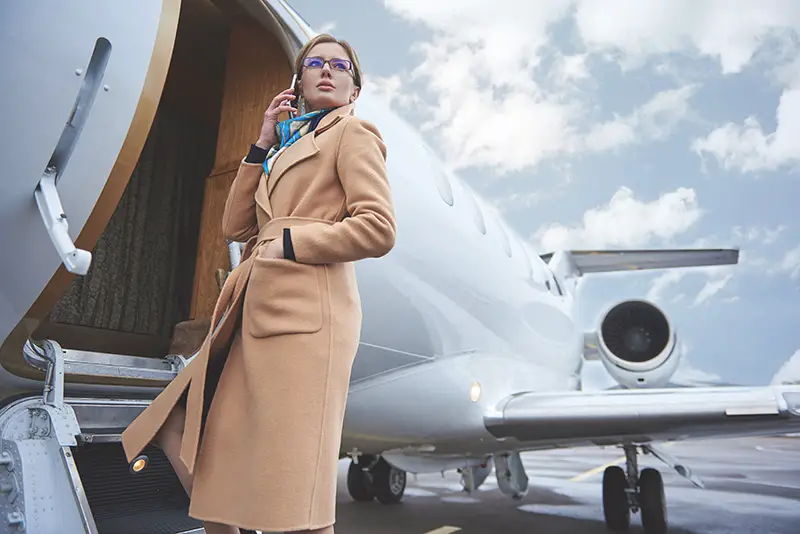 Low angle portrait of serene girl talking by phone while entering in aircraft. Career concept