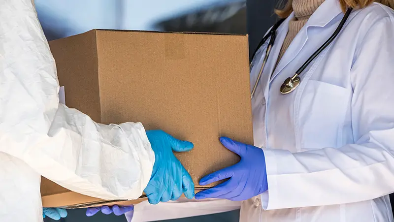 A person in a protective suit is handed a box of medicines to a doctor