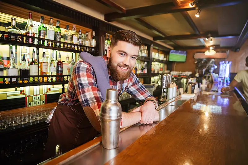 young bartender standing and smiling in bar