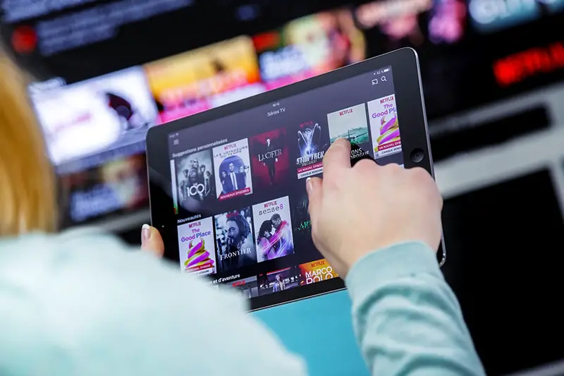 Woman Holding a touch pad and switching channels on France Netflix HomePage. with TV set on background.