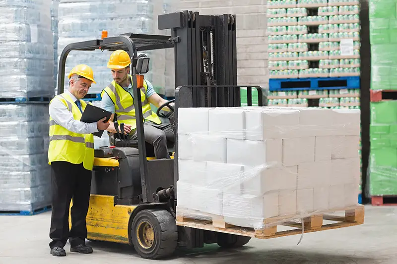 Forklift driver talking with his manager in a large warehouse