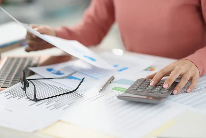 Business woman counting on calculator and holding documents in hands closeup