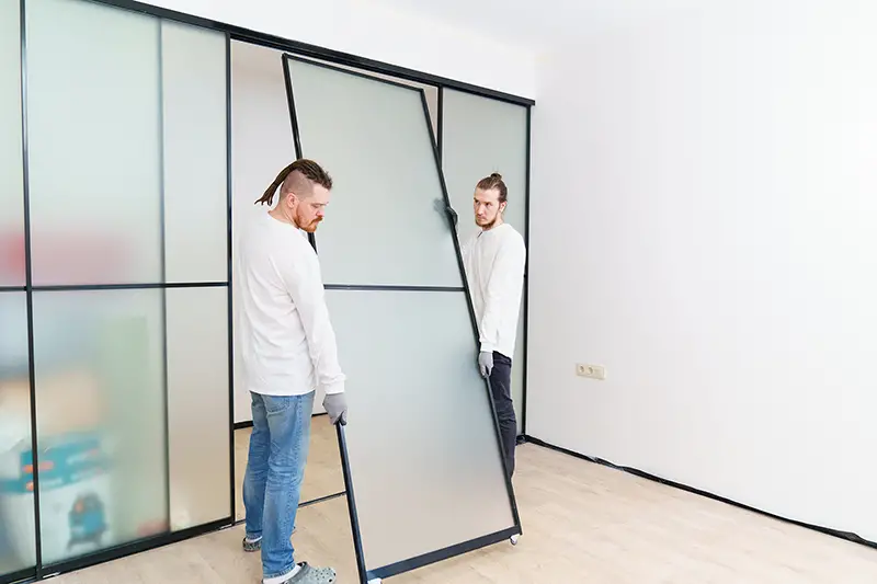 Men install the sliding doors of the wardrobe made of metal and glass