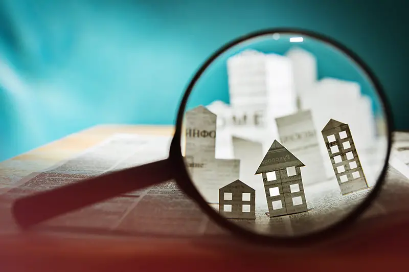 Magnifying glass in front of an open newspaper with paper houses