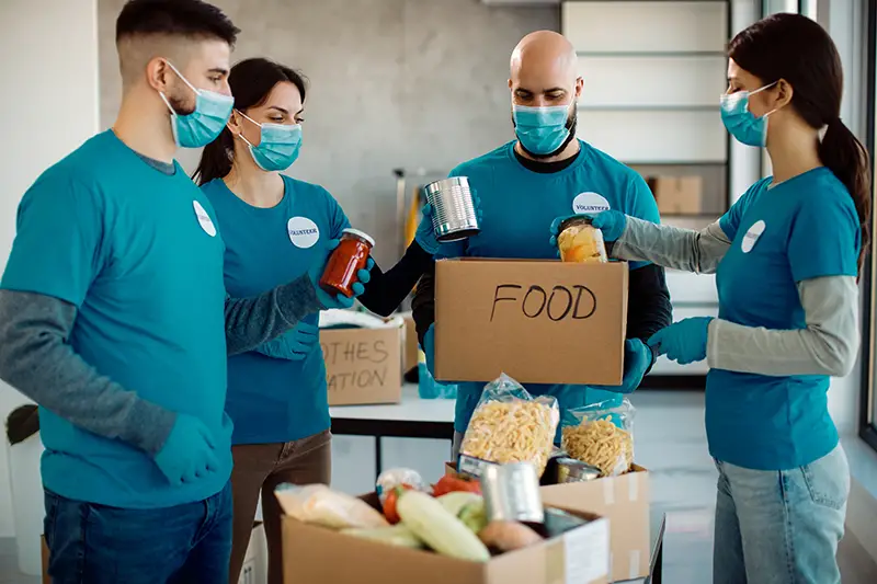 Group of people working in charitable foundation and packing food in donation boxes during COVID-19 pandemic.