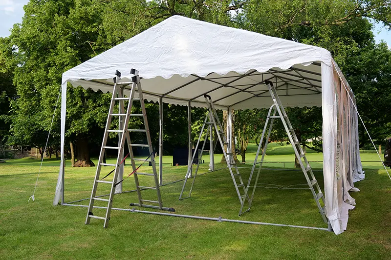 event tent set up  with ladders on the lawn in a park