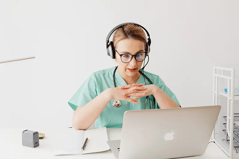 woman in scrub suit sitting in front of a laptop on a video call