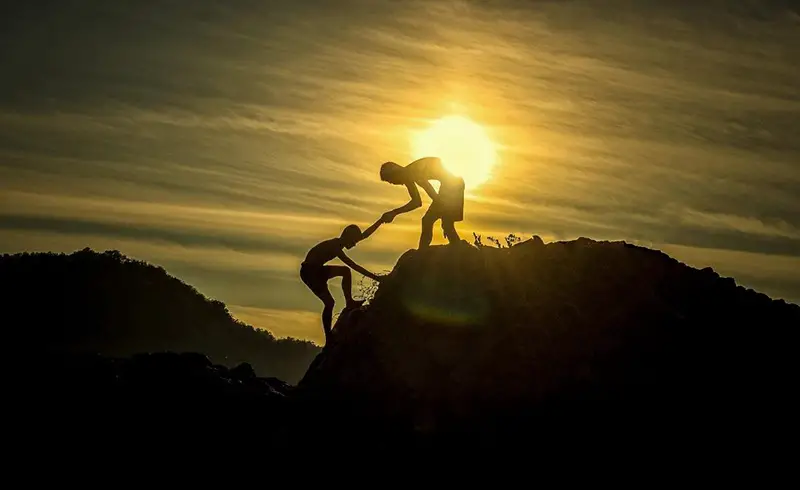 Person helping a hand in climbing a hill during sunset