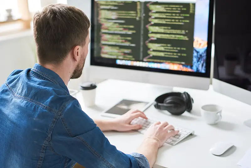 Back view portrait of contemporary web developer writing code for program sitting at desk and working on startup project in modern office, copy space