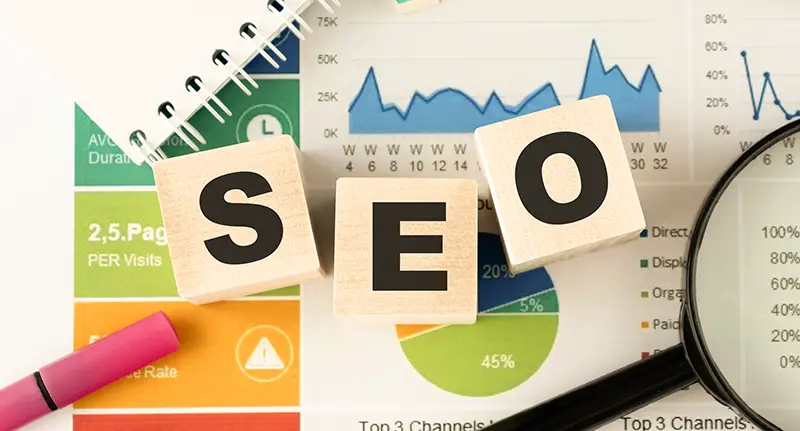 Three wooden cubes with letters SEO, on white table, more in background, space for text in right down corner