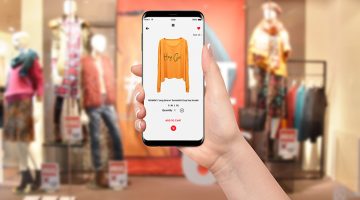 Woman In front of clothing store buying yellow hoodie online on her phone