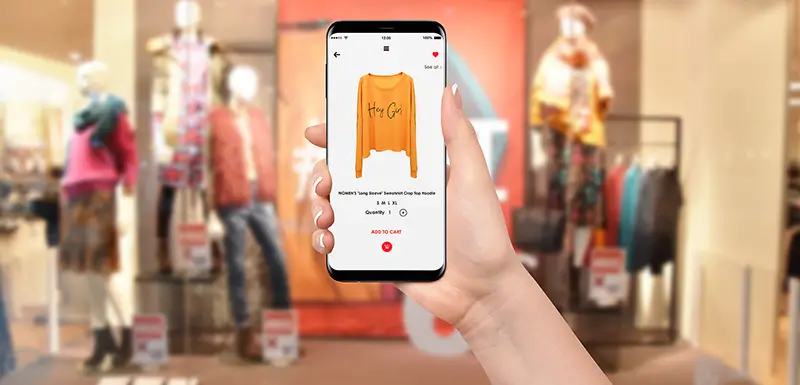Woman In front of clothing store buying yellow hoodie online on her phone