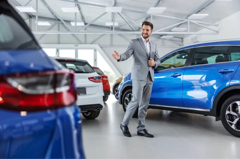 Friendly car seller in suit walking around car salon and showing around cars