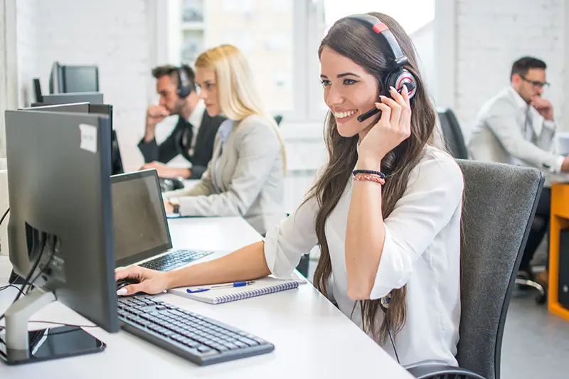 Smiling woman call center operator with headset using computer
