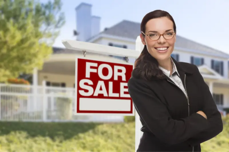 Woman real estate agent standing in front of house for sale sign