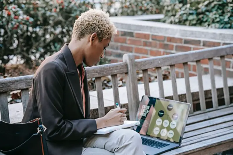 Woman working on her laptop sitting on wooden bench