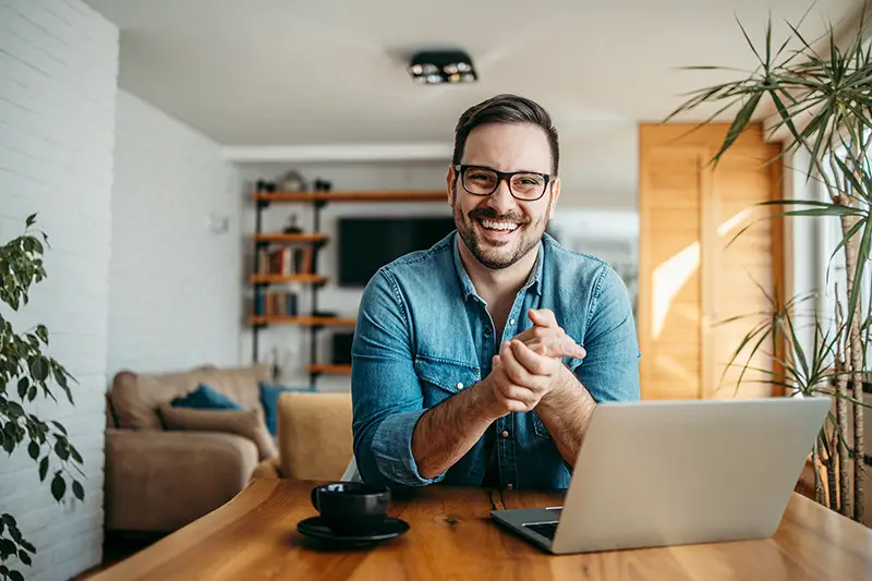 Man smiling in front of his working desk and laptop