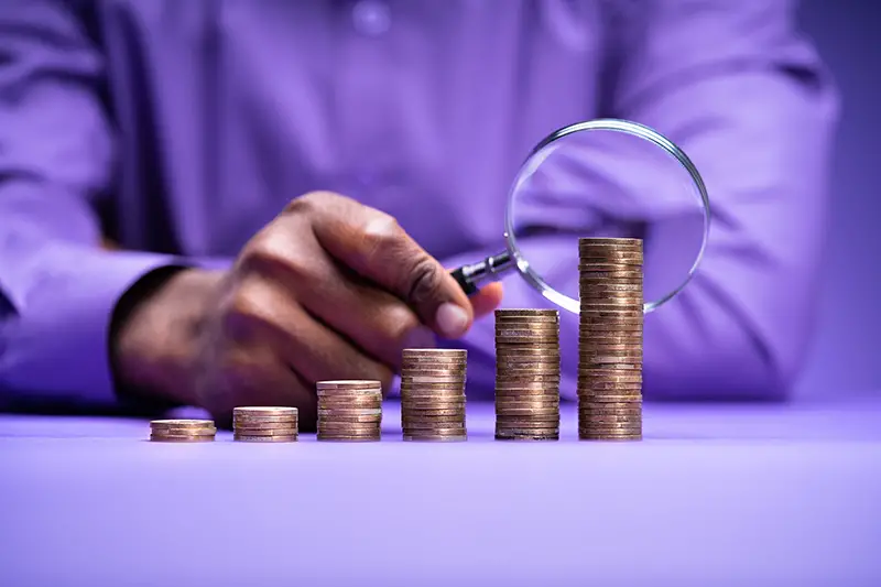 Man using magnifying glass through pile of coins