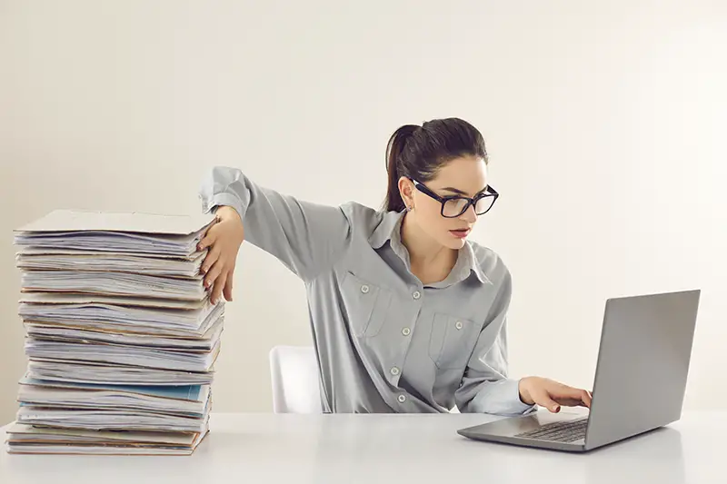 Young woman working on  her laptop beside the documents pile