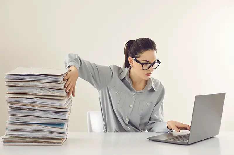 Young woman working on her laptop beside the documents pile