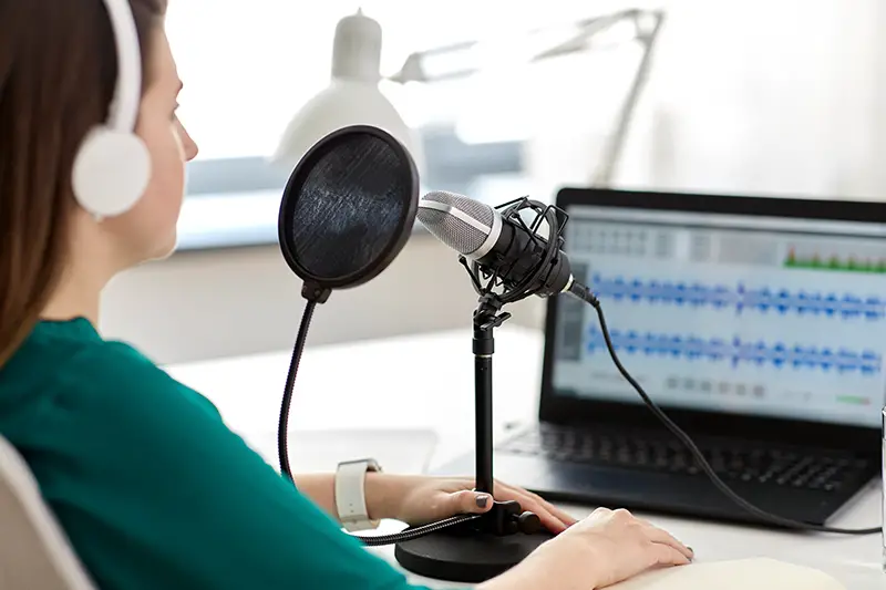 Woman using microphone and laptop computer talking and recording at studio