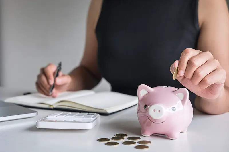 Woman putting golden coin in pink piggy bank