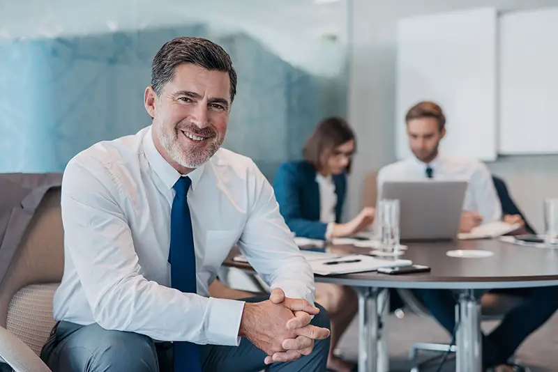 Portrait of a confident mature businessman wearing a shirt and tie sitting at a table in an office