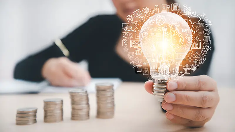 Woman hand hold light bulb with icons work on the desk