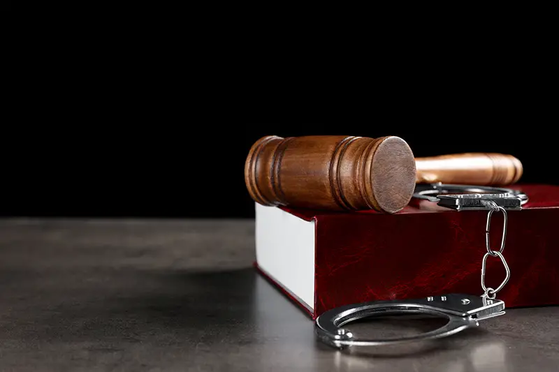 Judge's gavel, handcuffs and book on grey table
