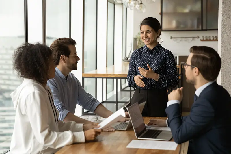 Smiling Indian businesswoman leading corporate meeting with diverse colleagues