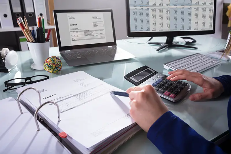 Businessperson's Hand Calculating Invoice At Workplace