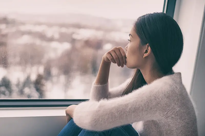 Sad young woman sitting near the glass window