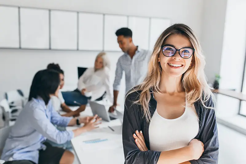 Blonde female executive posing with smile and arms crossed during brainstorm with managers