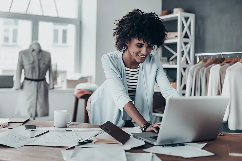 Beautiful young African woman working using computer and smiling while standing in workshop