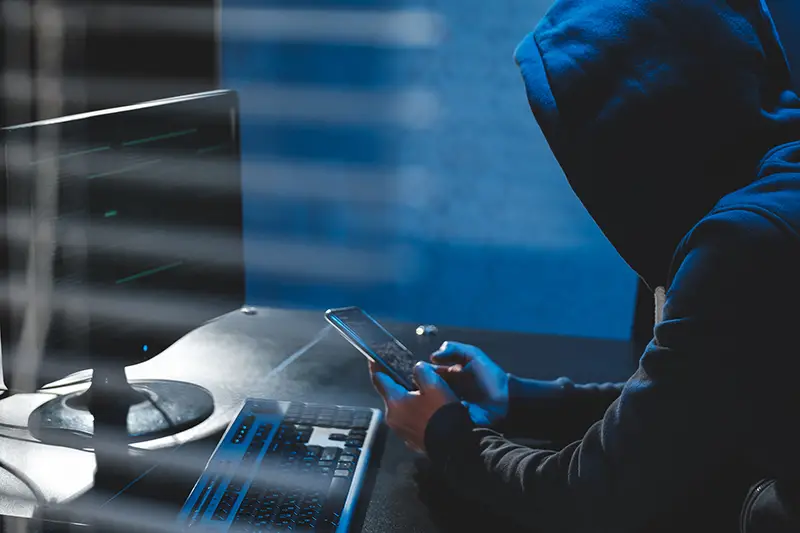 Overhead hacker in hood working at computer and mobile phone