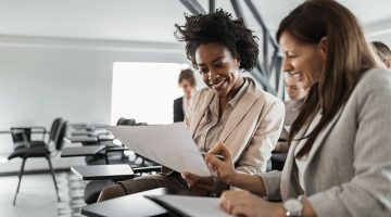 Two females in a suits, doing paper work.
