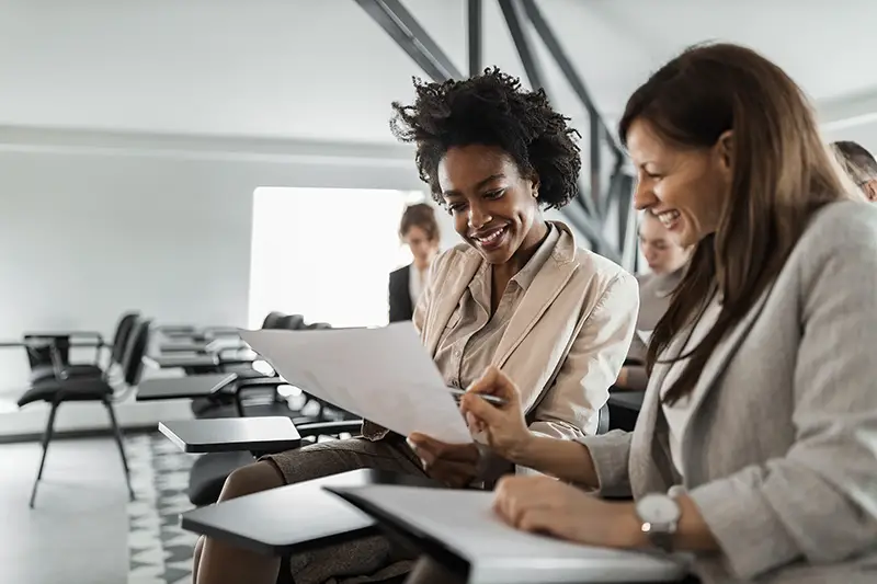 Two females in a suits, doing paper work.