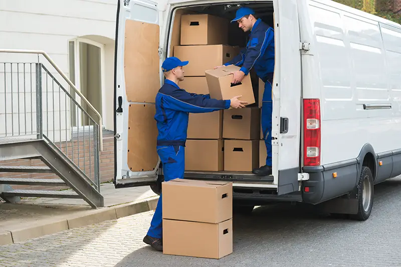 Young delivery men unloading cardboard boxes from truck