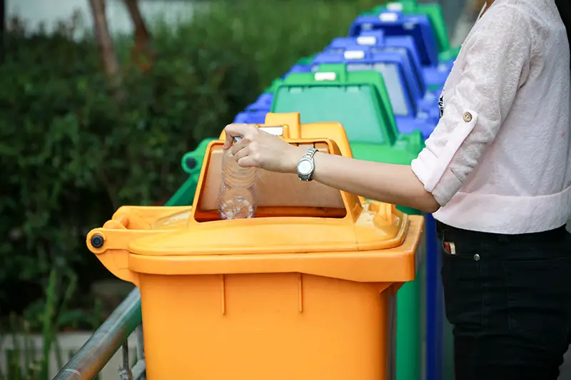 a woman dump a plastic bottle garbage to yellow recycle bin