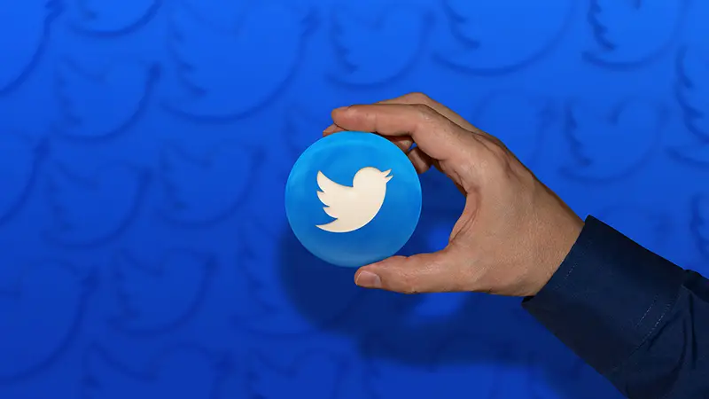 A hand holding a twitter logo glossy badge over blue background