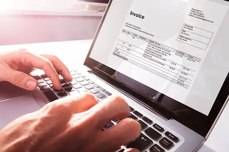Close-up Of Businessman's Hands Working On Invoice On Laptop At Office